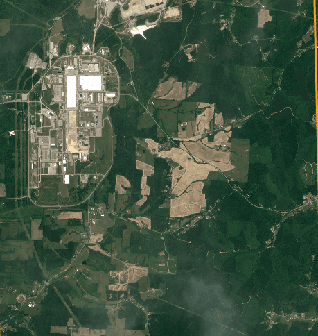 Satellite view of the former Portsmouth Gaseous Diffusion Plant in Piketon, Ohio on June 24, 2026: the large white process buildings and paved yards of the existing plant at left, ringed by a perimeter road, with farmland, woodland and open fields covering the surrounding acreage where the PORTS Technology Campus is planned.
